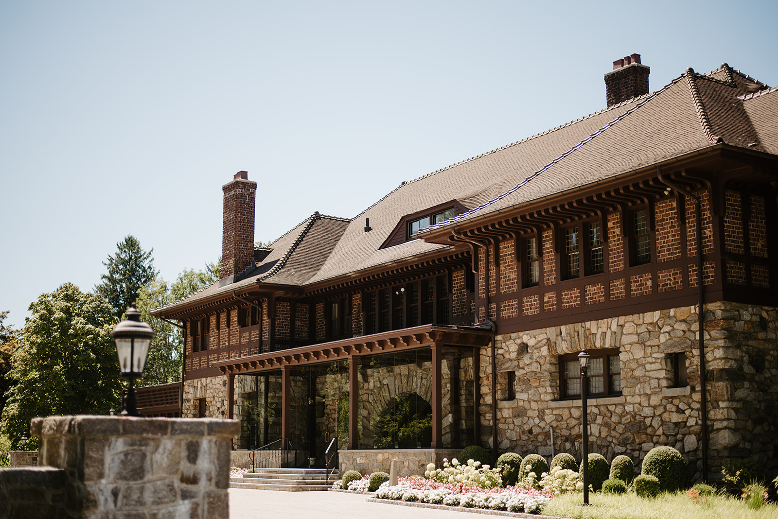 Sunny exterior view of Le Chateau mansion's stone walls, timber framing, and manicured gardens.